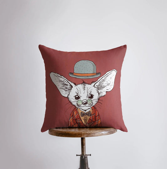 Decorative pillow with a fox illustration wearing a hat and coat on a wooden stool against a light gray background.